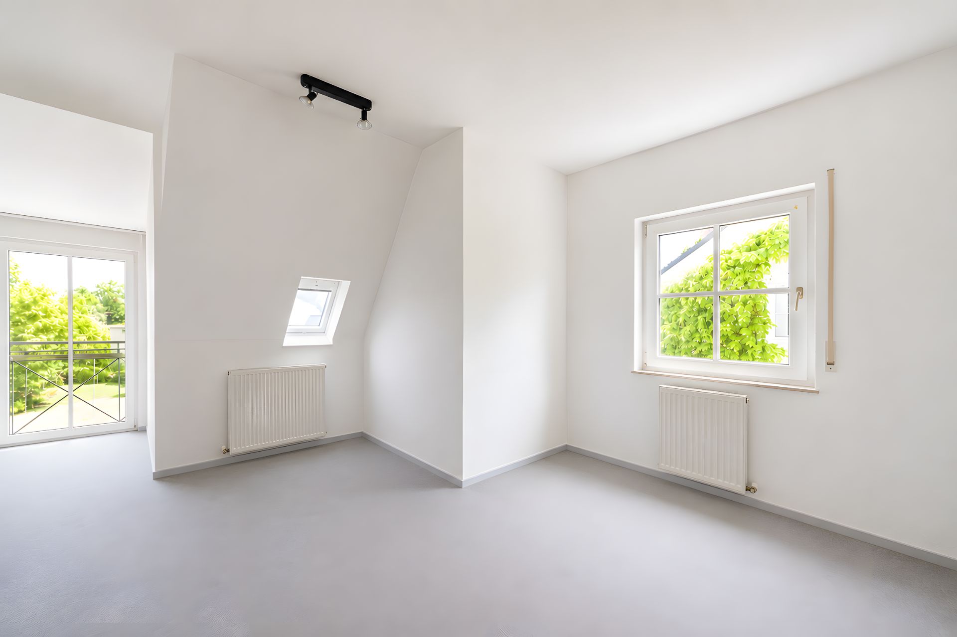 Helles, leeres Zimmer mit weißen Wänden, zwei Fenstern und zwei Heizkörpern.