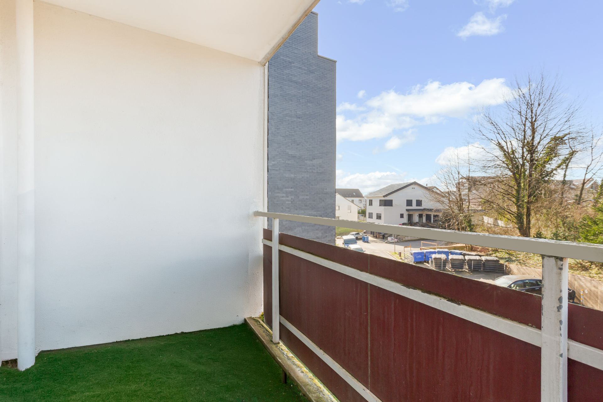 Balkon mit grünem Bodenbelag und Ausblick auf Wohnhäuser und Bäume.