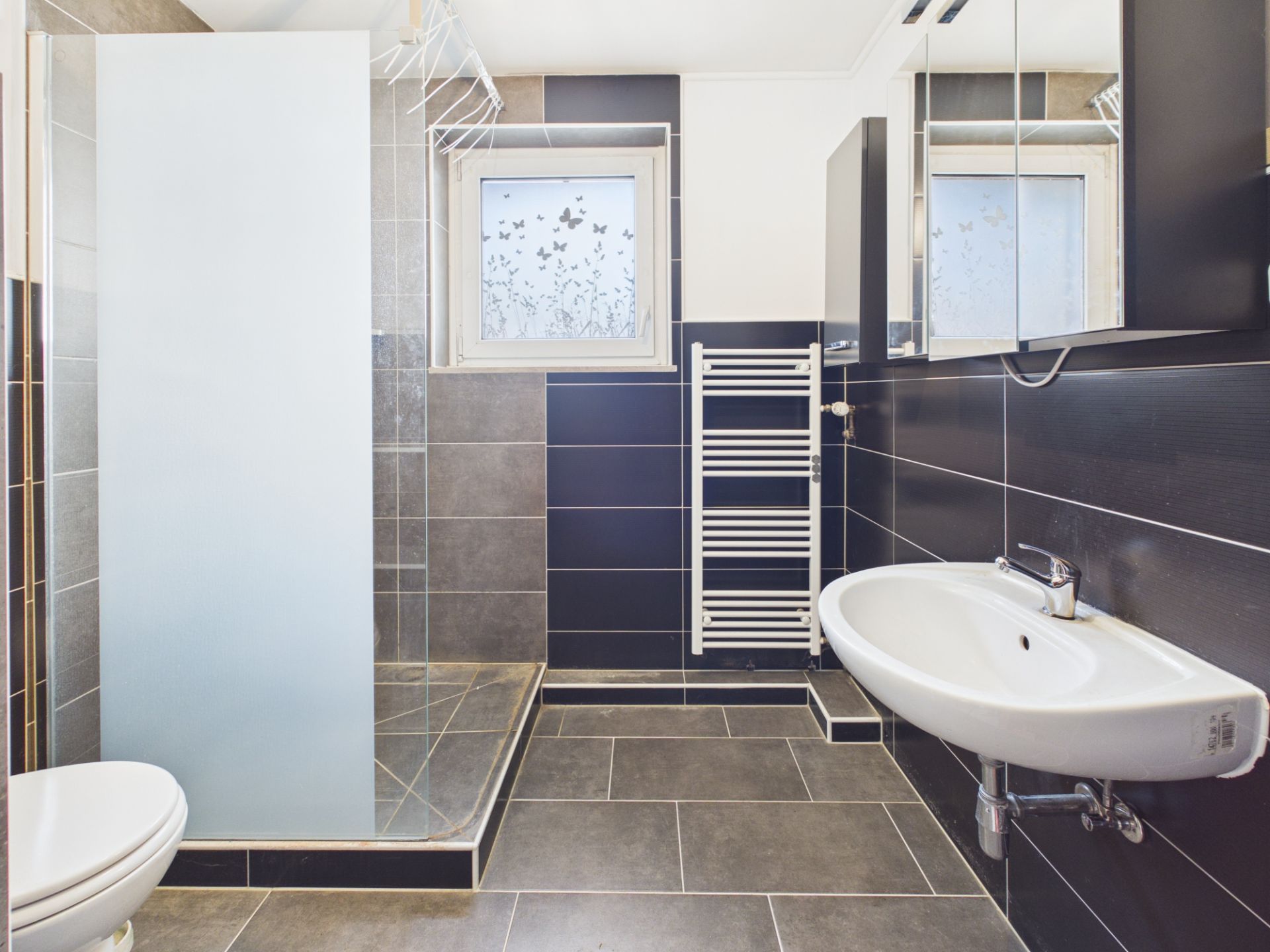 Modernes Badezimmer mit ebenerdiger Dusche, Waschbecken und Handtuchheizkörper.