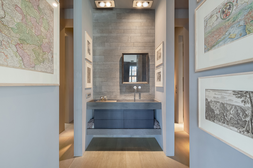Modernes Badezimmer mit grauem Waschbecken, Spiegel und gerahmten Bildern an den Wänden.