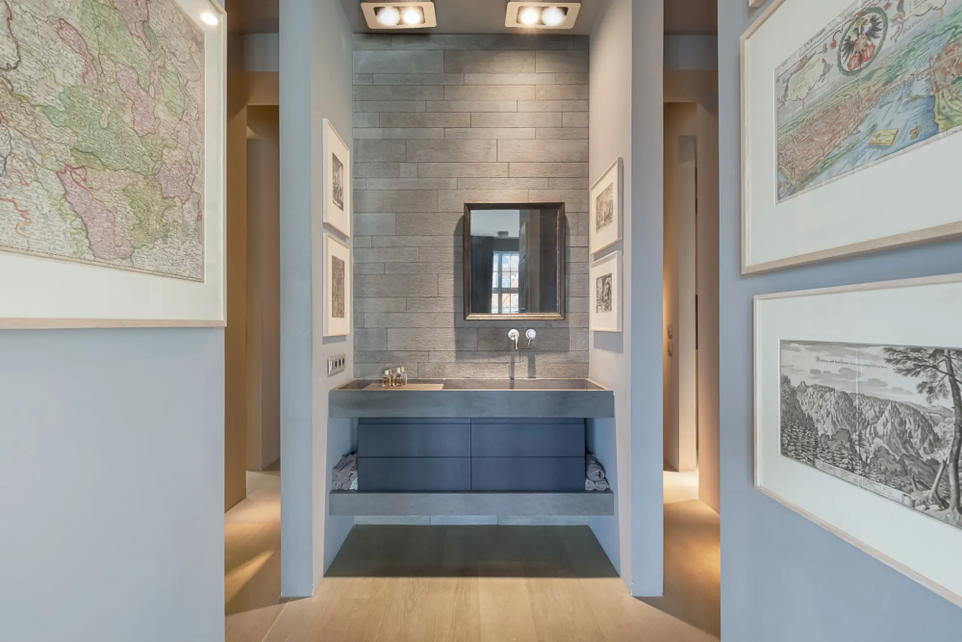 Modernes Badezimmer mit grauem Waschbecken, Spiegel und gerahmten Bildern an den Wänden.