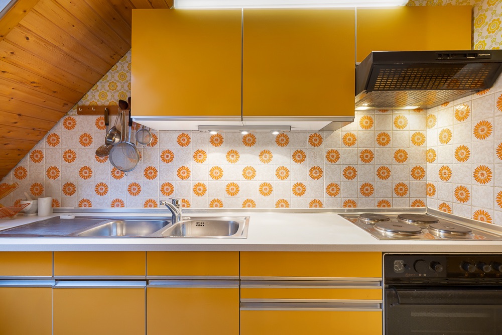 Küche mit gelben Schränken, Spüle, Herd und gemusterten Fliesen an der Wand.