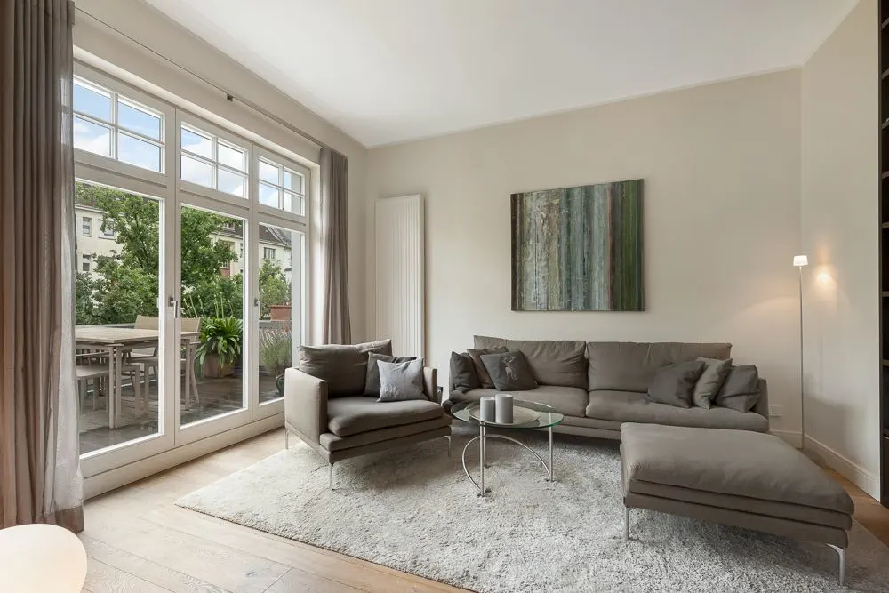 Modernes Wohnzimmer mit grauem Sofa, Glastisch, Teppich und großen Fenstern zu einem Balkon.