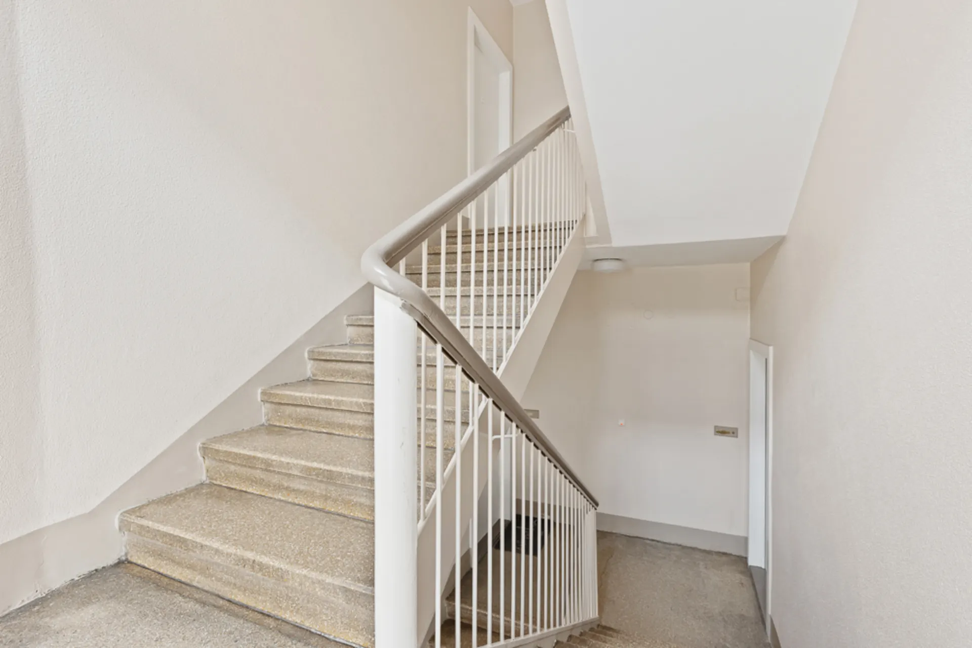 Helles Treppenhaus mit Betontreppe und weißem Geländer in einem Wohngebäude.