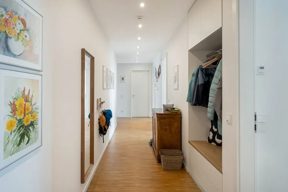 Heller Flur mit Holzboden, Garderobe, Spiegel, Bildern und Kommode.