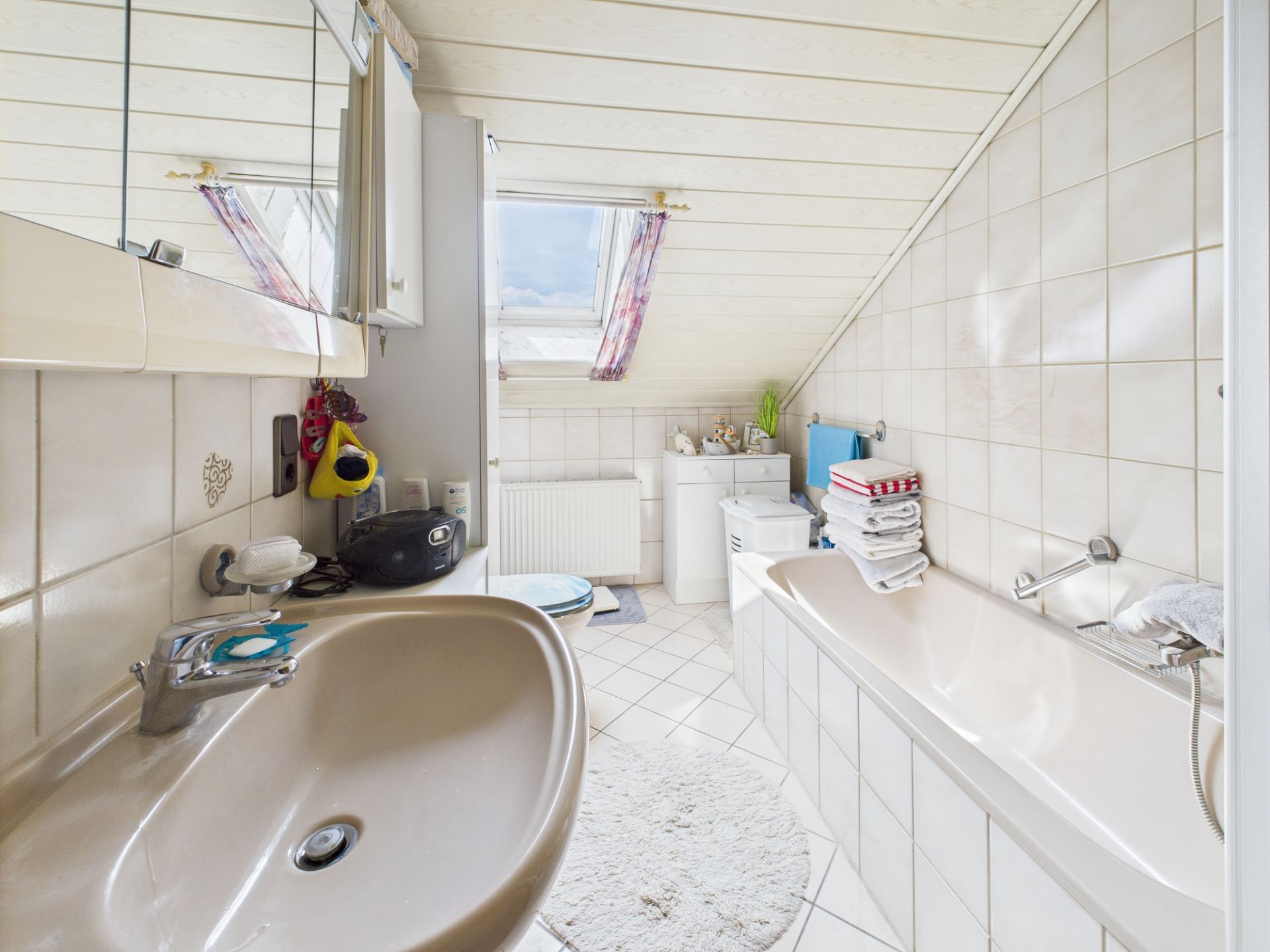 Helles Badezimmer mit Waschbecken, Badewanne, Dachfenster und weißen Fliesen.