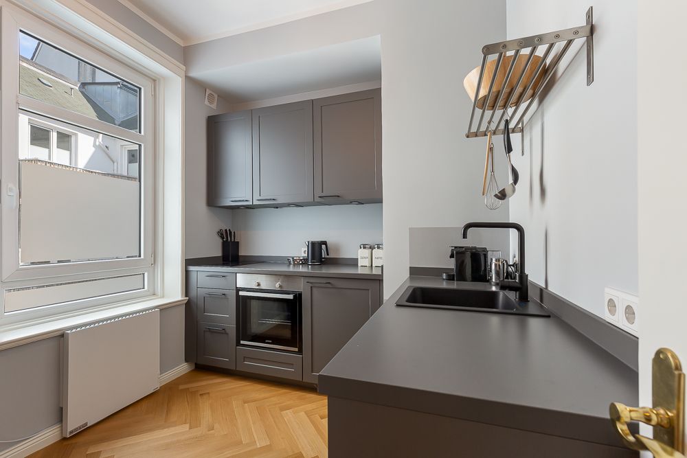 Moderne Küche mit grauen Schränken, großem Fenster und Parkettboden.