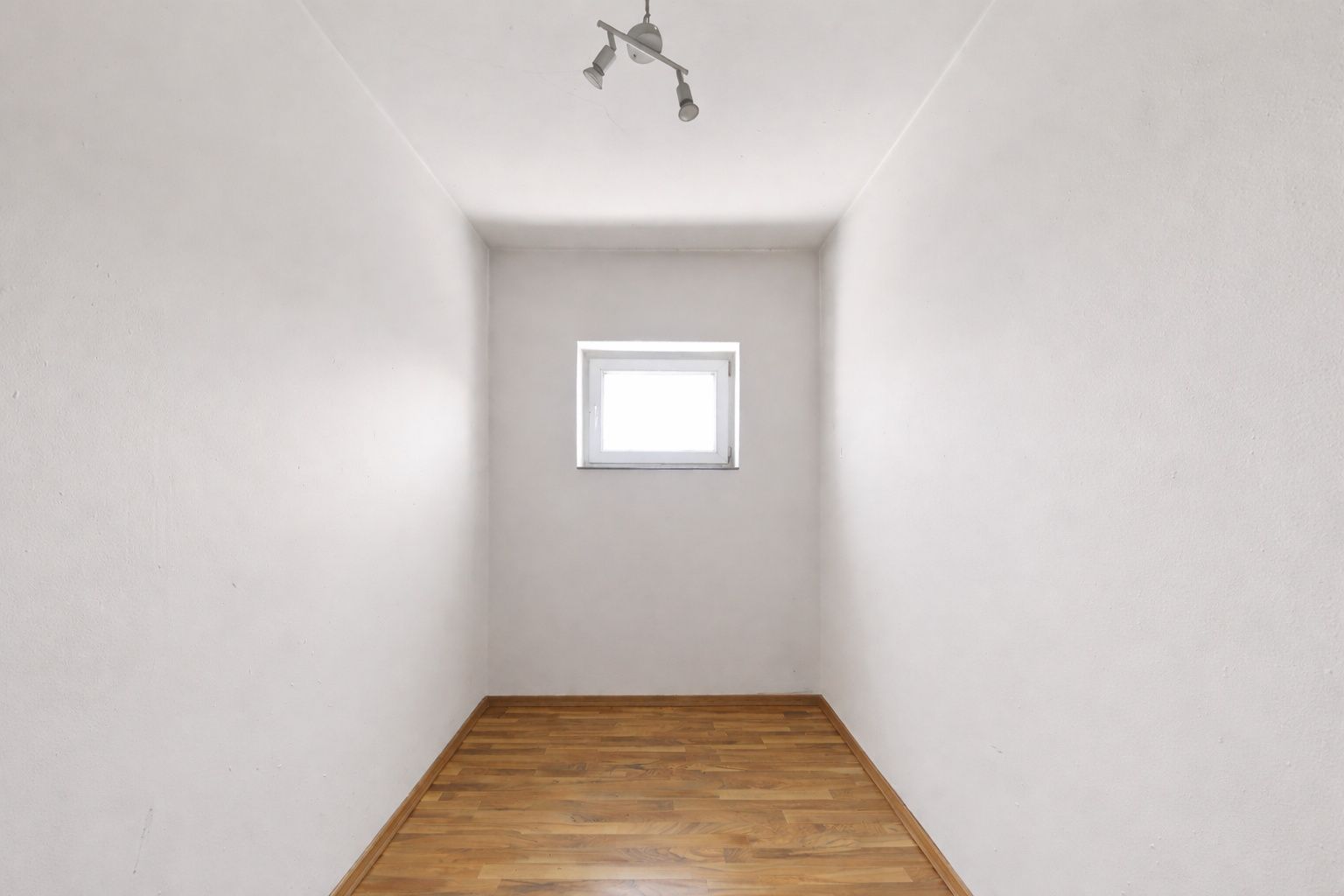 Kleiner leerer Raum mit Holzboden, weiß gestrichenen Wänden und einem Fenster an der Stirnseite.