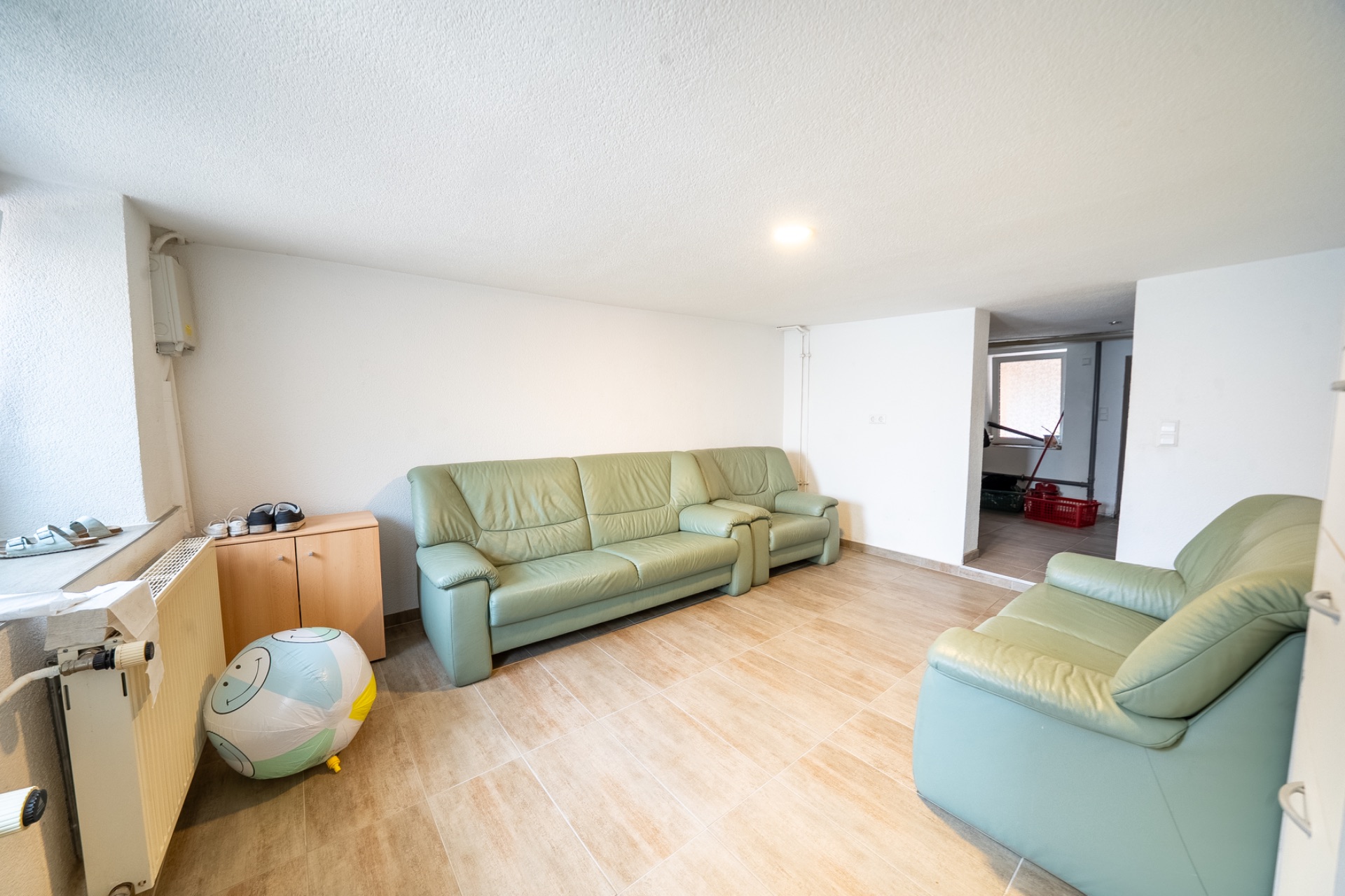 Wohnzimmer mit zwei grünen Sofas, einem Sessel, einem Schrank und Ball auf hellem Holzboden.