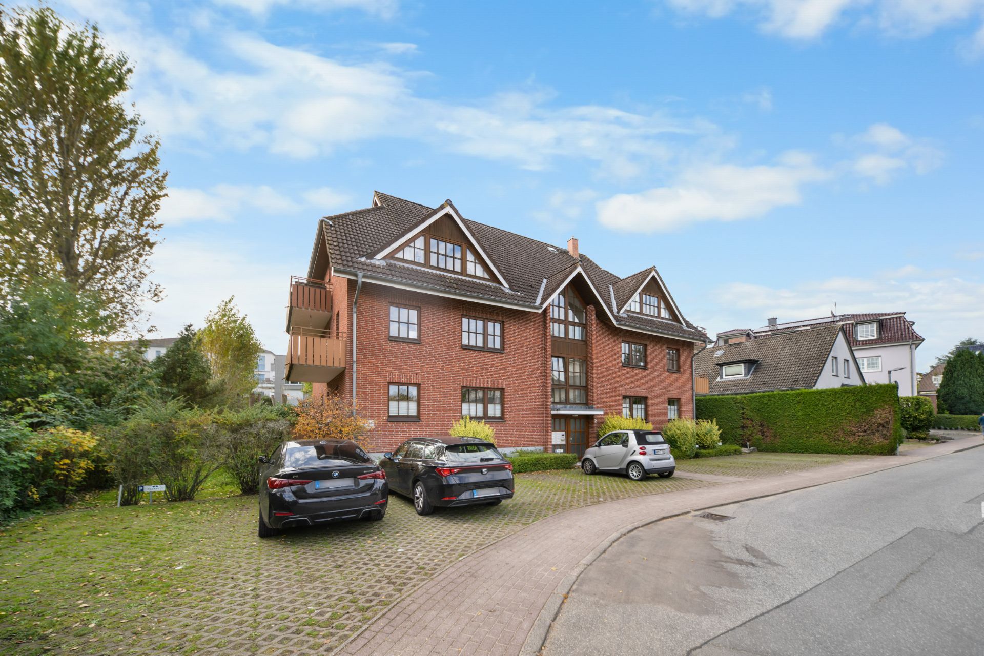 Mehrfamilienhaus aus rotem Backstein mit mehreren geparkten Autos und bepflanztem Vorgarten.