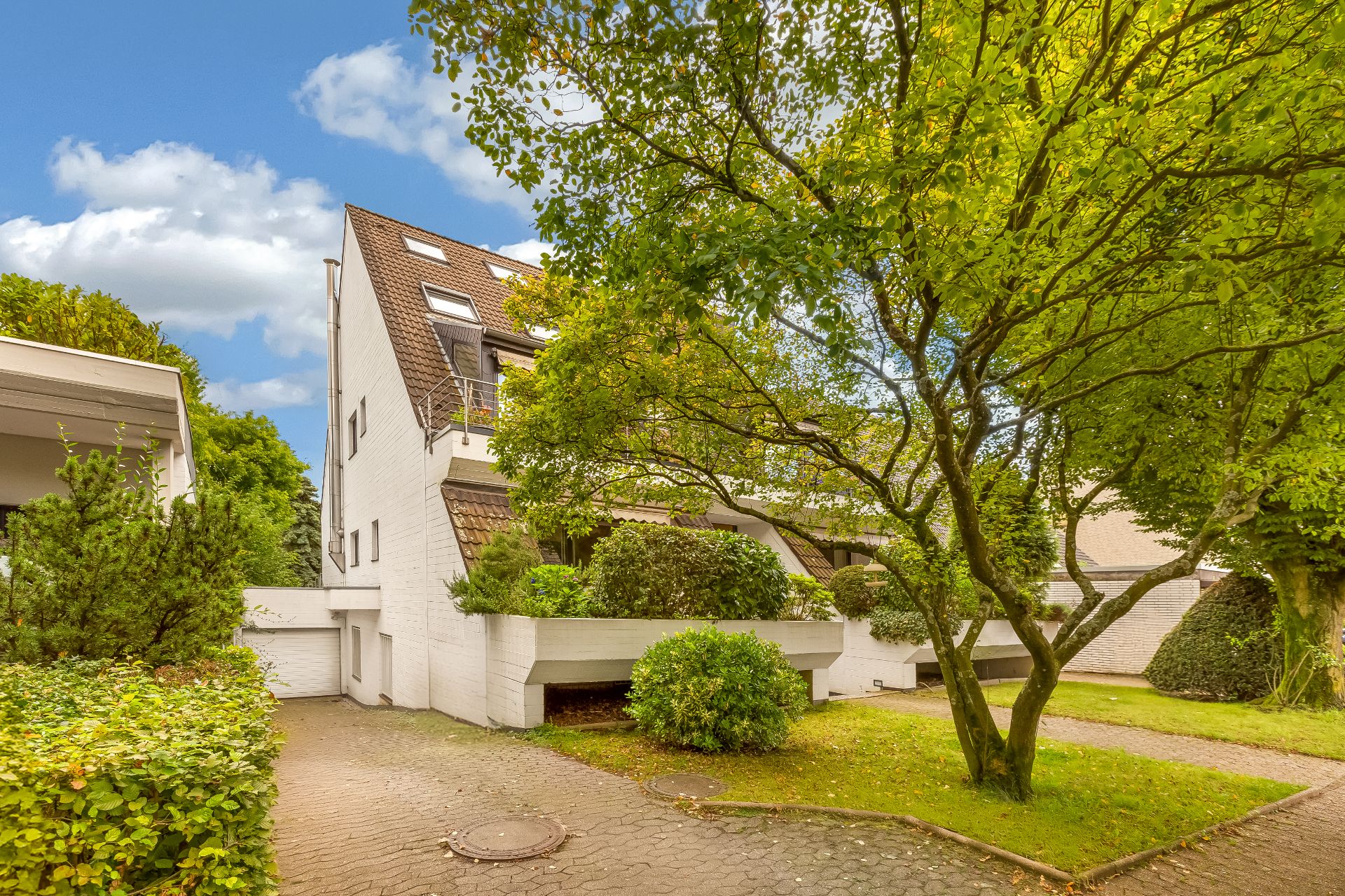 Mehrfamilienhaus mit weißer Fassade, Vorgarten und Bäumen an einem sonnigen Tag.