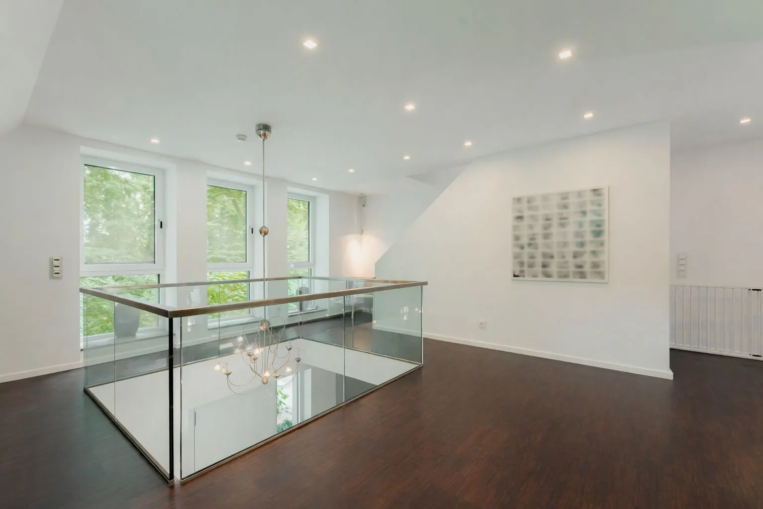 Heller Raum mit Glasgeländer, dunklem Holzboden und drei großen Fenstern.