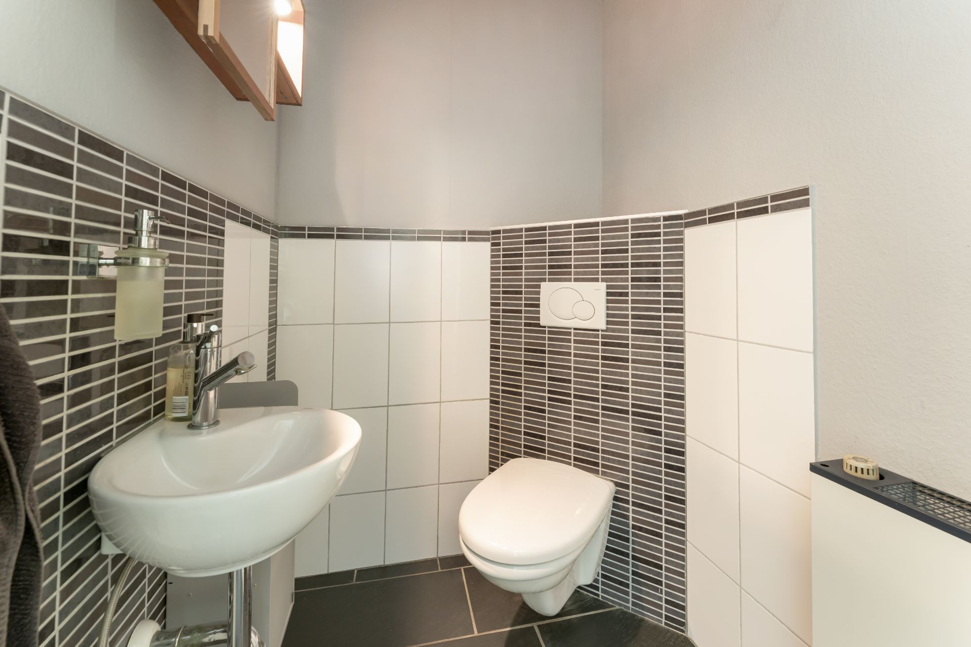 Kleines Bad mit Wand-WC, Waschbecken und dunklem Fliesenboden.