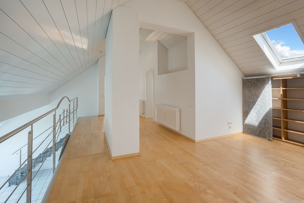 Heller Dachgeschossraum mit Holzfußboden, Dachfenster und Treppengeländer.