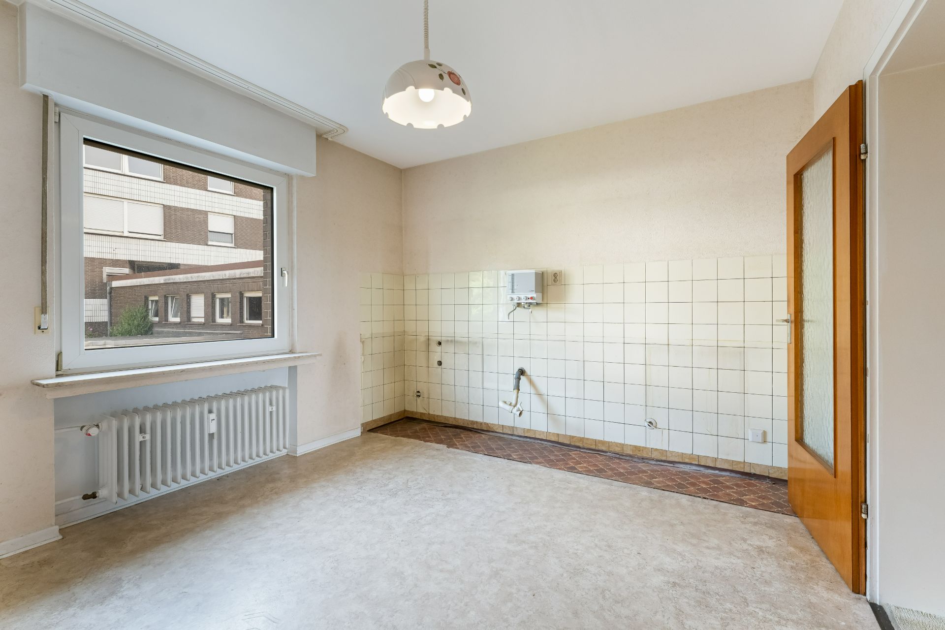 Leerer Raum mit Fliesenspiegel, Fenster, Heizung und offener Holztür, ohne Möbel.