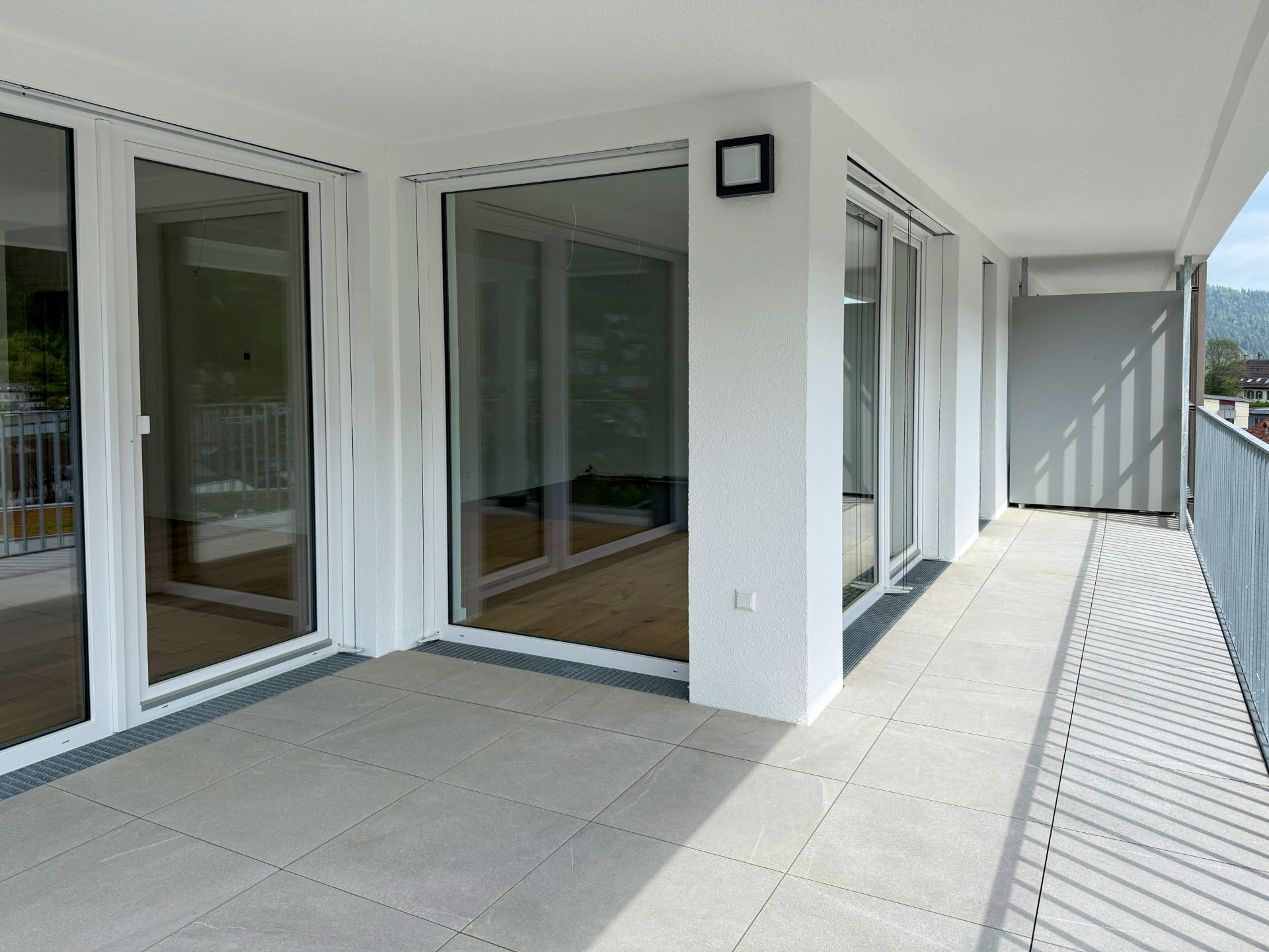 Großer, überdachter Balkon mit Fliesenboden und bodentiefen Fenstern.