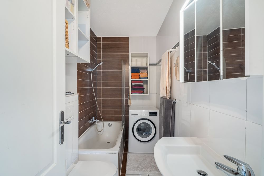 Modernes Badezimmer mit Badewanne, Waschmaschine, Spiegel und Regalen mit Handtüchern.