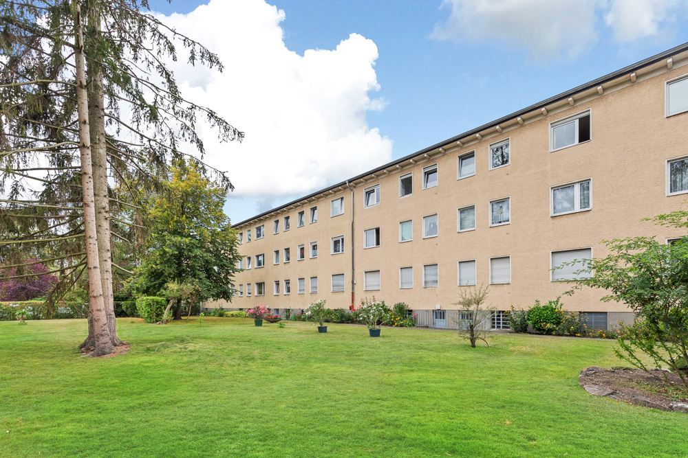Mehrfamilienhaus mit drei Etagen und großem begrünten Garten im Vordergrund.