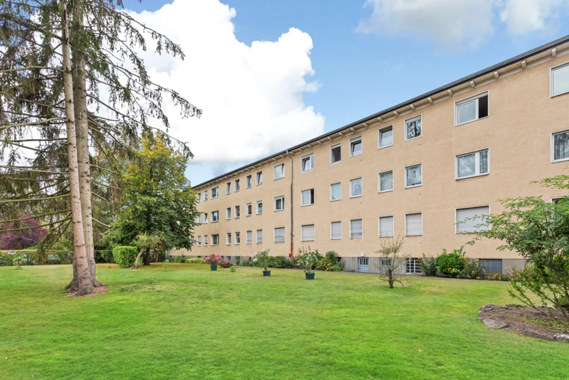 Mehrfamilienhaus mit drei Etagen und großem begrünten Garten im Vordergrund.