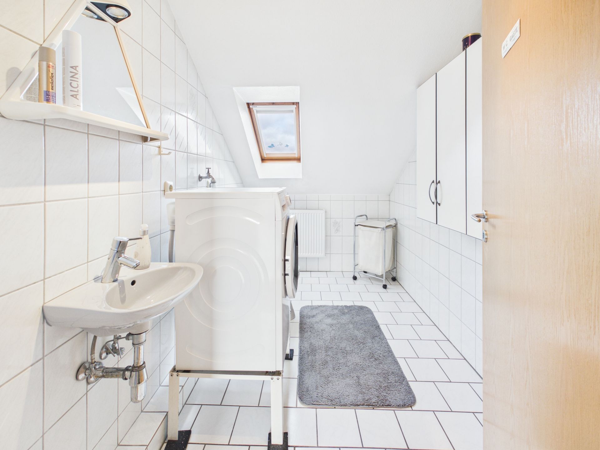 Heller Hauswirtschaftsraum mit Waschmaschine, Waschbecken, Schränken und Dachfenster.