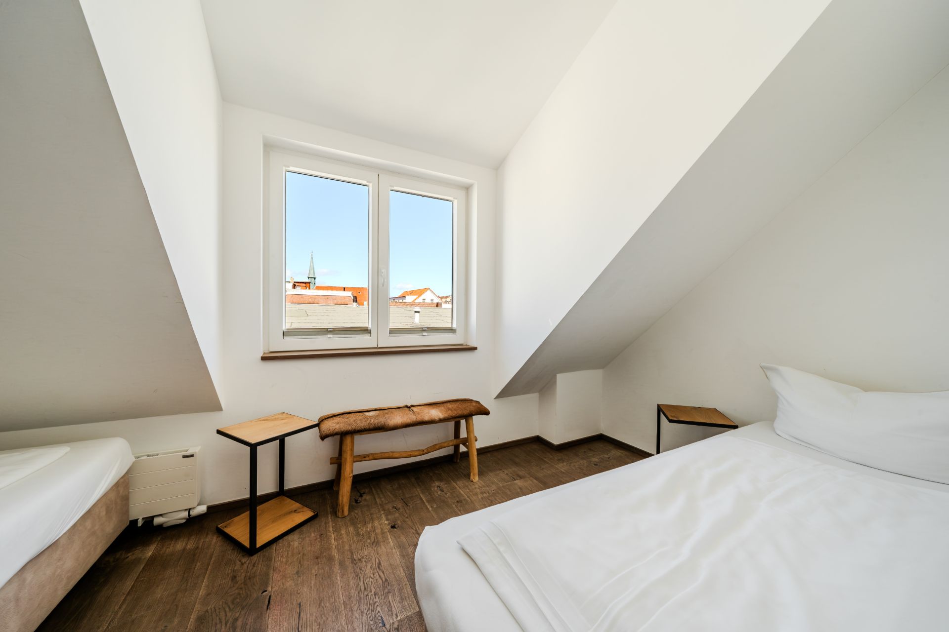 Helles Schlafzimmer mit zwei Betten, Holzbank und Dachfenster in einem Dachgeschoss.