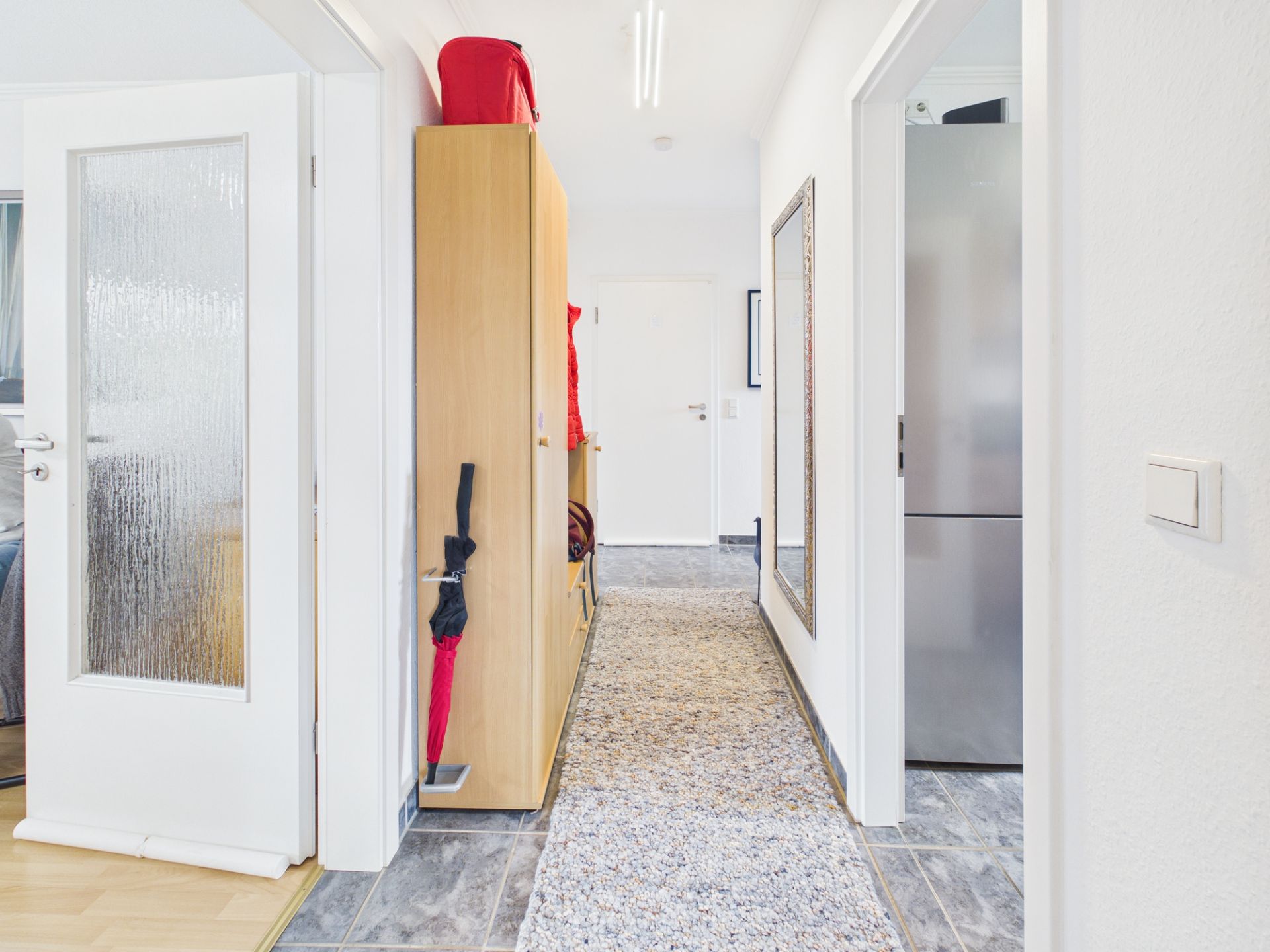 Heller Flur mit Spiegel, Garderobe, Teppich und offenen Türen zu anderen Zimmern.