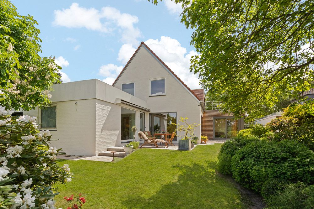 Modernes Einfamilienhaus mit Terrasse und Garten, umgeben von Bäumen und Blumen.