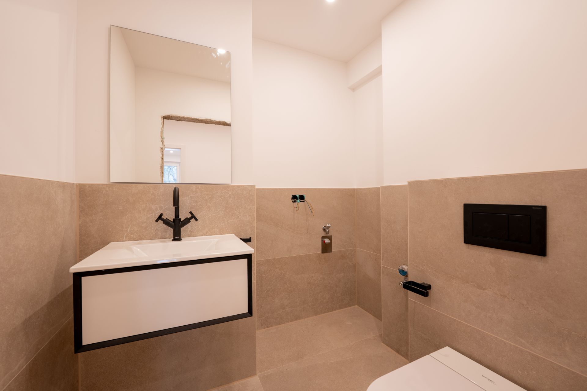 Modernes Badezimmer mit Waschbecken, Spiegel und Toilette, beige Wandfliesen.