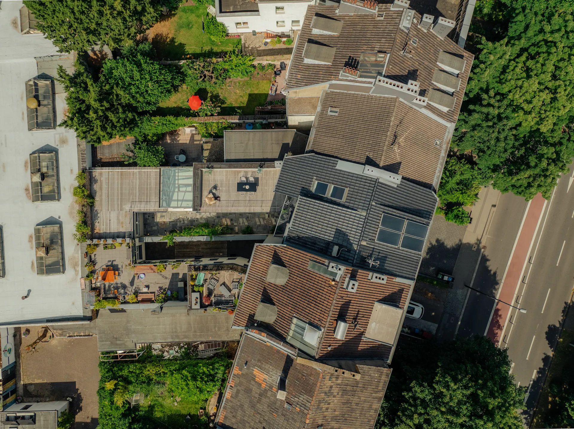 Luftaufnahme von Wohnhäusern mit begrünten Höfen und Terrassen an einer Straße.