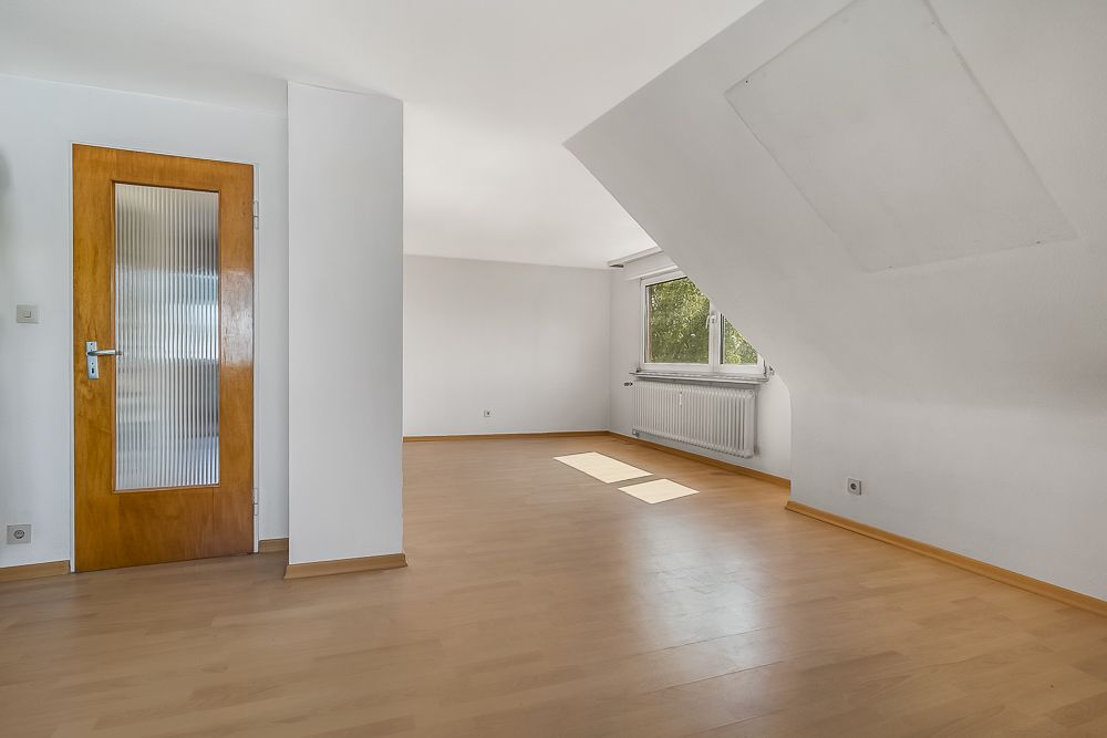 Helles, leeres Zimmer mit Holzfußboden, weißer Wand, Fenster und Holztür.
