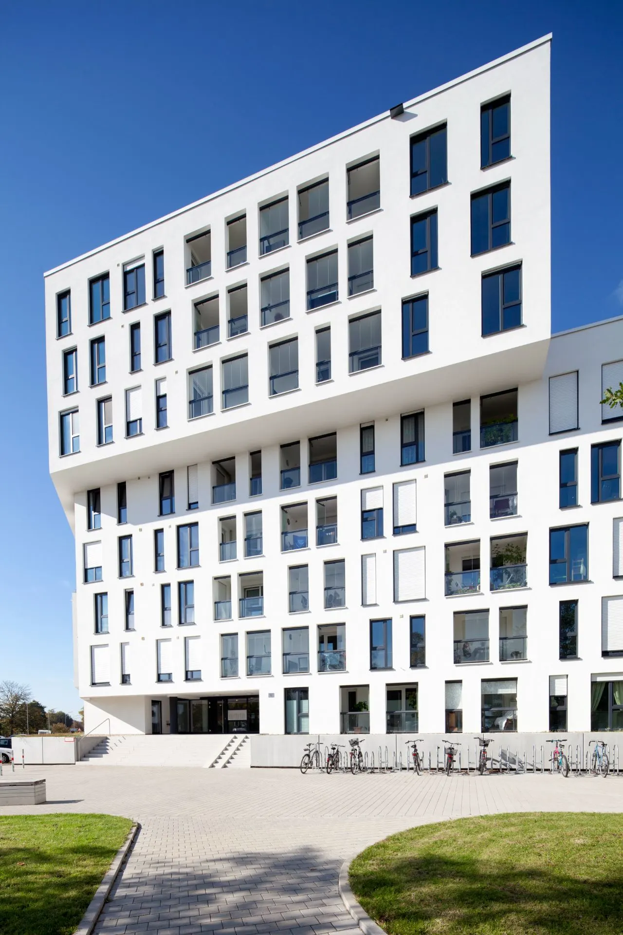 Modernes Wohnhaus mit vielen Fenstern und Fahrrädern im Eingangsbereich.