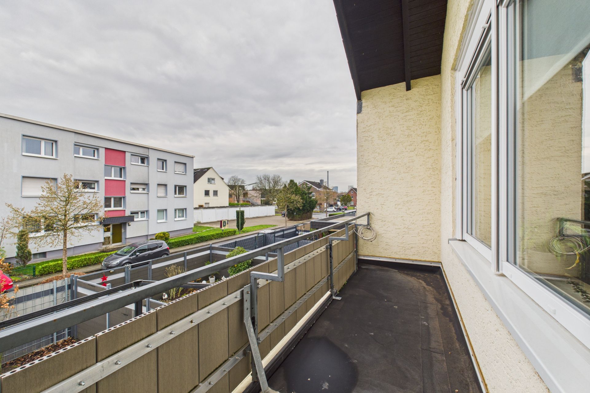 Balkon mit Geländer an einem Wohnhaus, Blick auf Straße und Nachbarhäuser.
