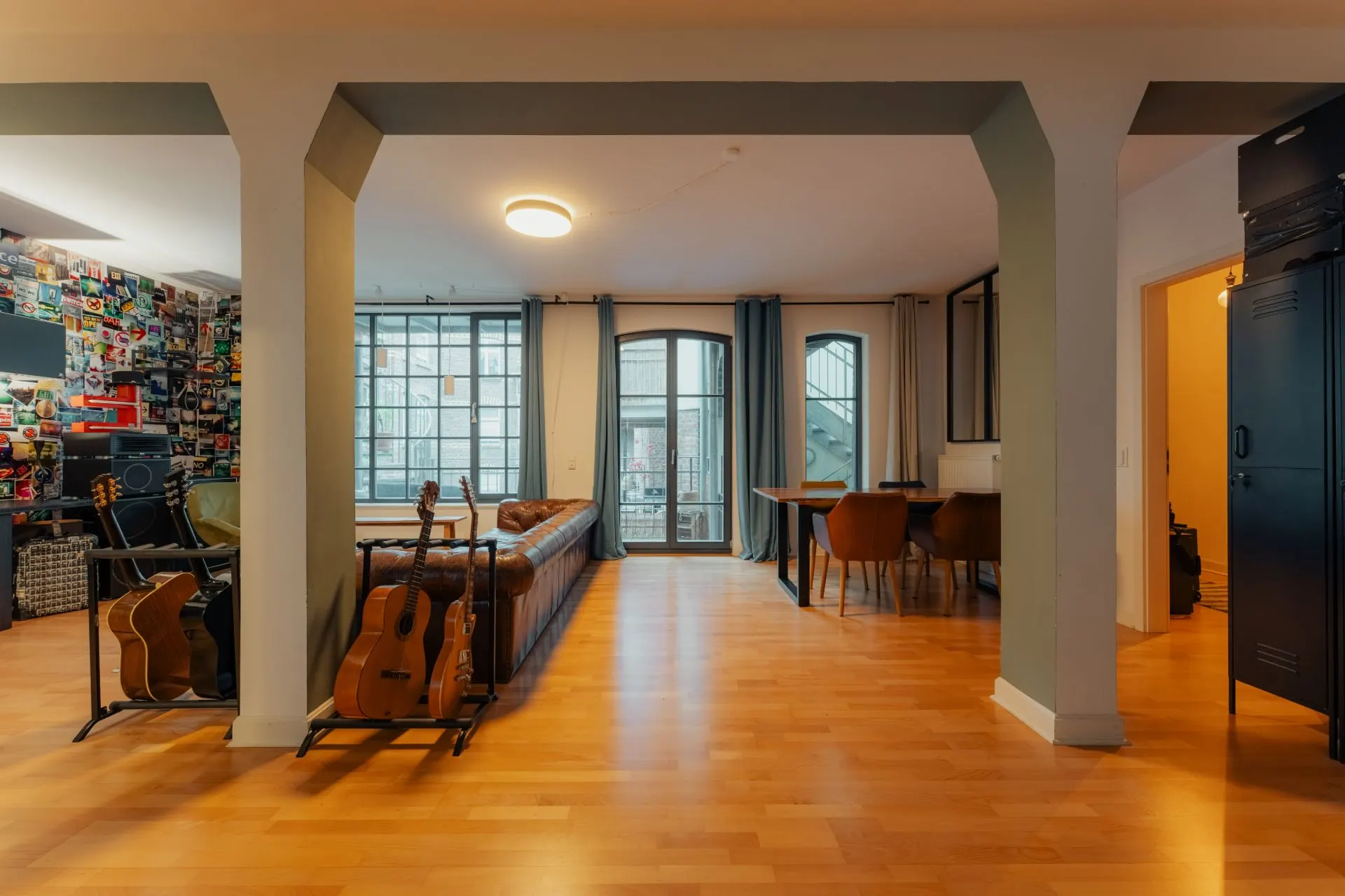 Wohnzimmer mit Ledersofa, mehreren Gitarren, großem Fenster und Essbereich mit Tisch und Stühlen.