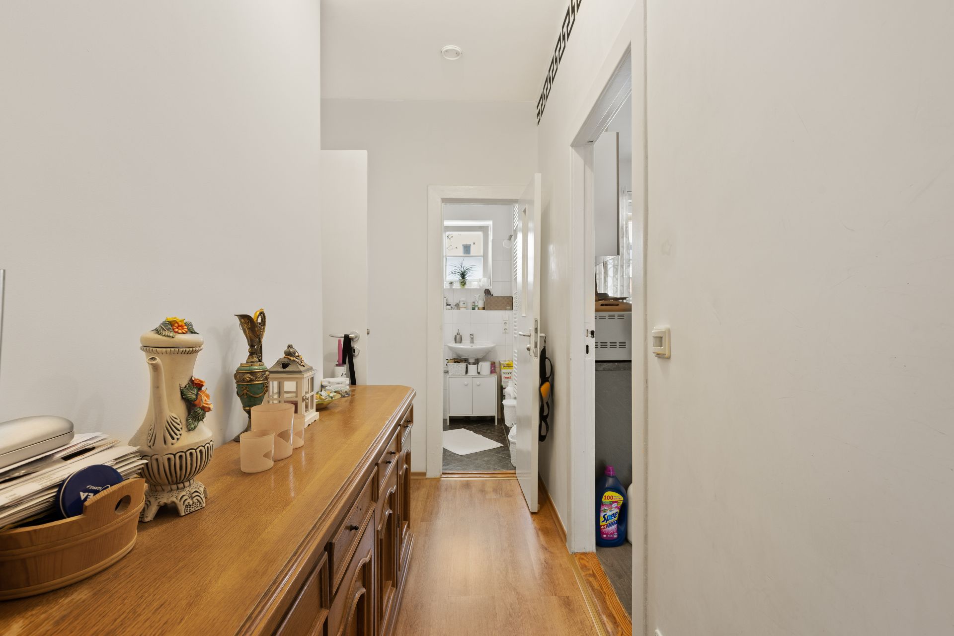 Flur mit Holzkommode und Dekoration, Blick ins Badezimmer und einen Nebenraum.