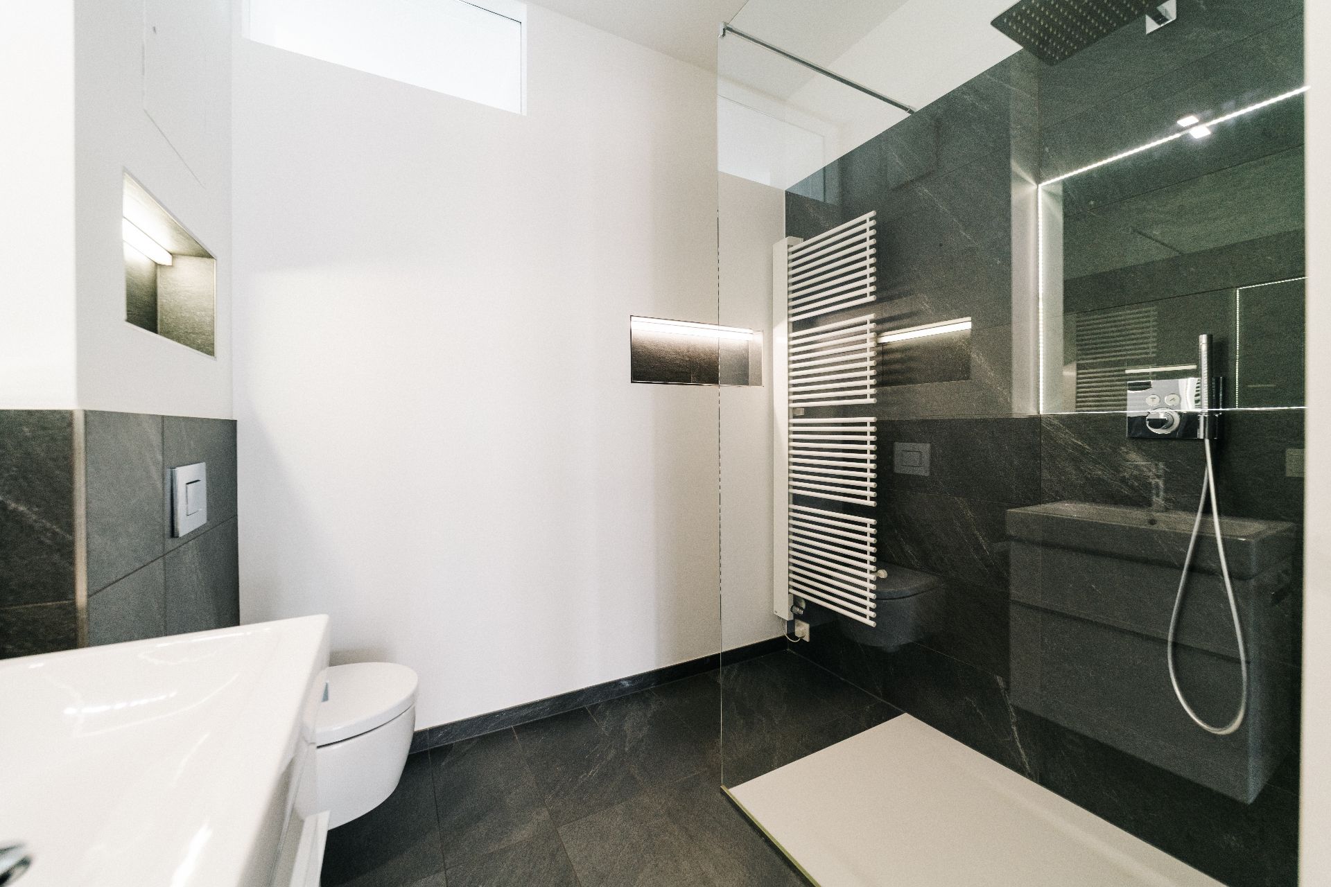 Modernes Badezimmer mit begehbarer Dusche, weißem WC und Waschbecken, dunklem Fliesenboden.