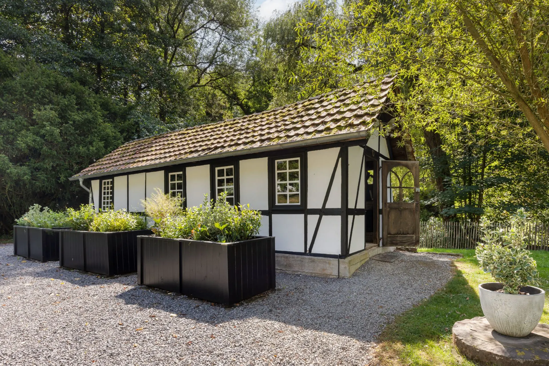 Kleines Fachwerkhaus mit Satteldach und mehreren Pflanzkübeln im Garten.
