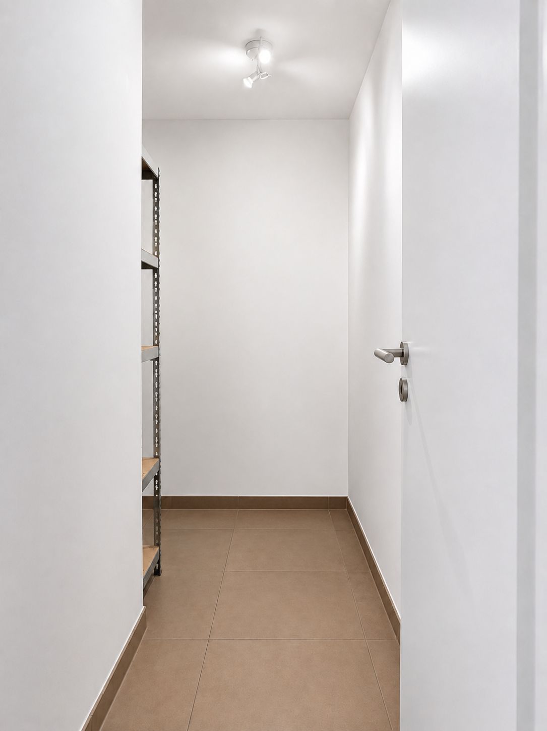 Kleiner, leerer Raum mit braunem Fliesenboden und Regal an der linken Wand.