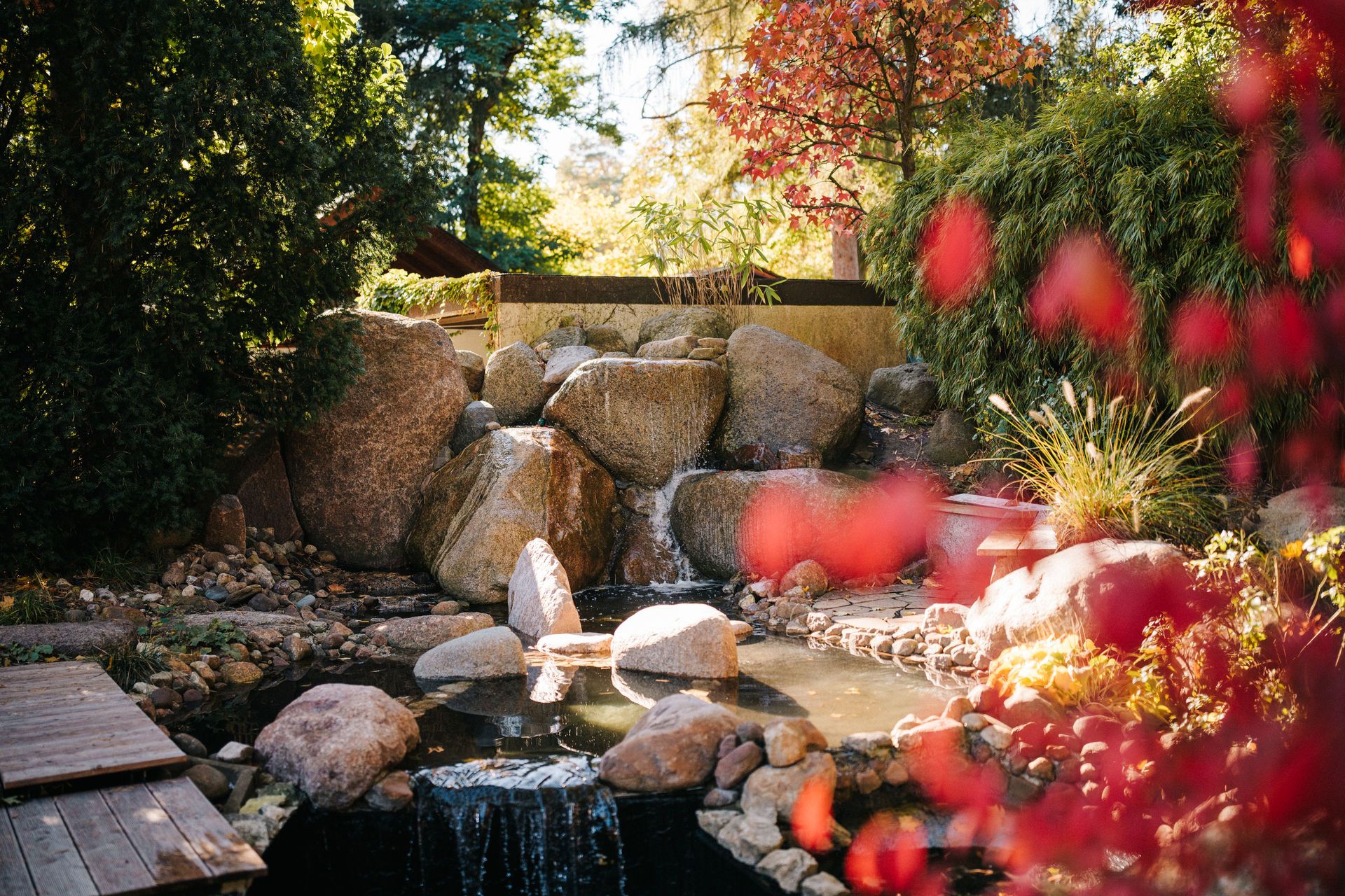 Garten mit großem Steingarten, Wasserfall und Teich, umgeben von Bäumen und Sträuchern.