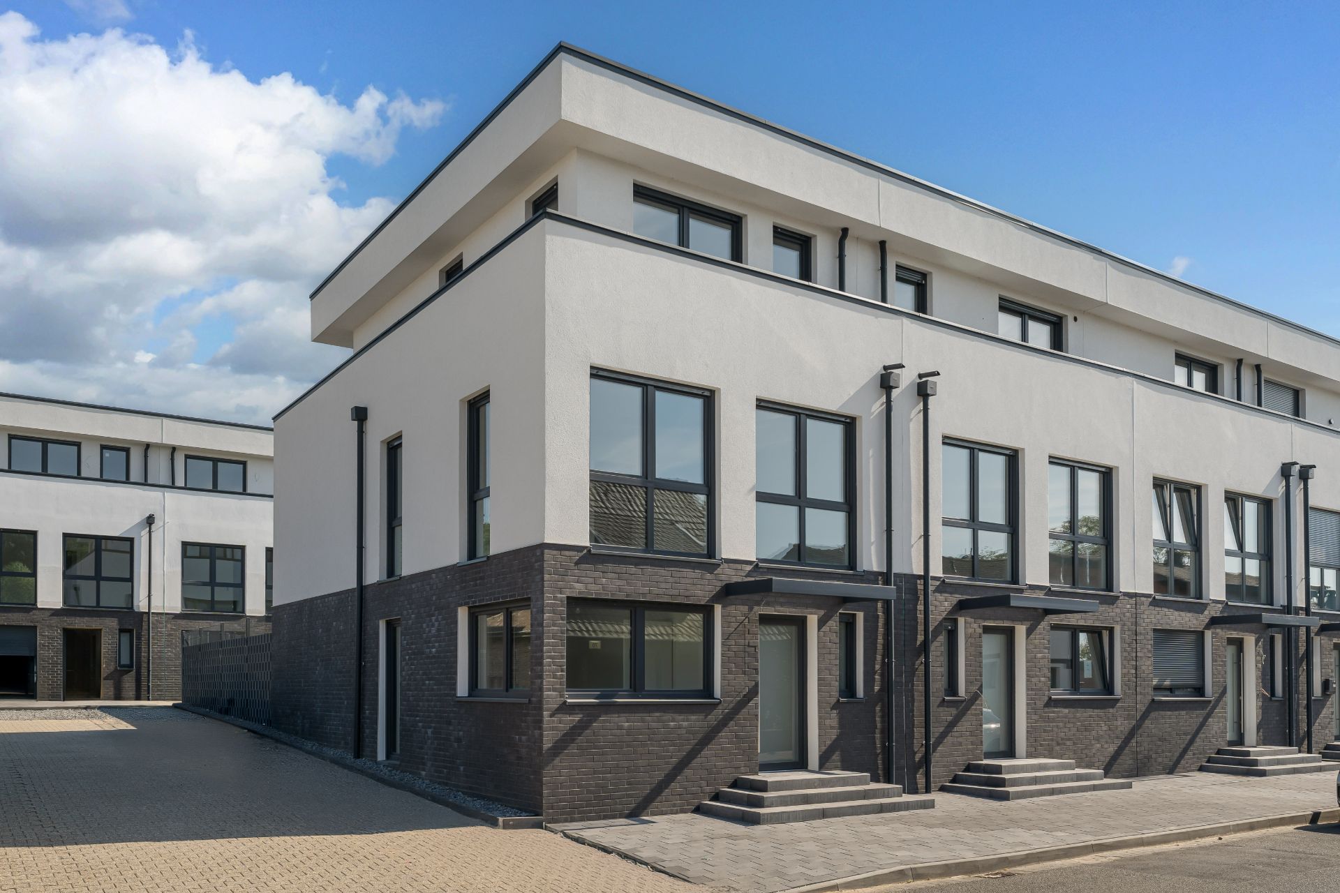 Modernes, dreistöckiges Wohngebäude mit großen Fenstern und mehreren Eingängen.