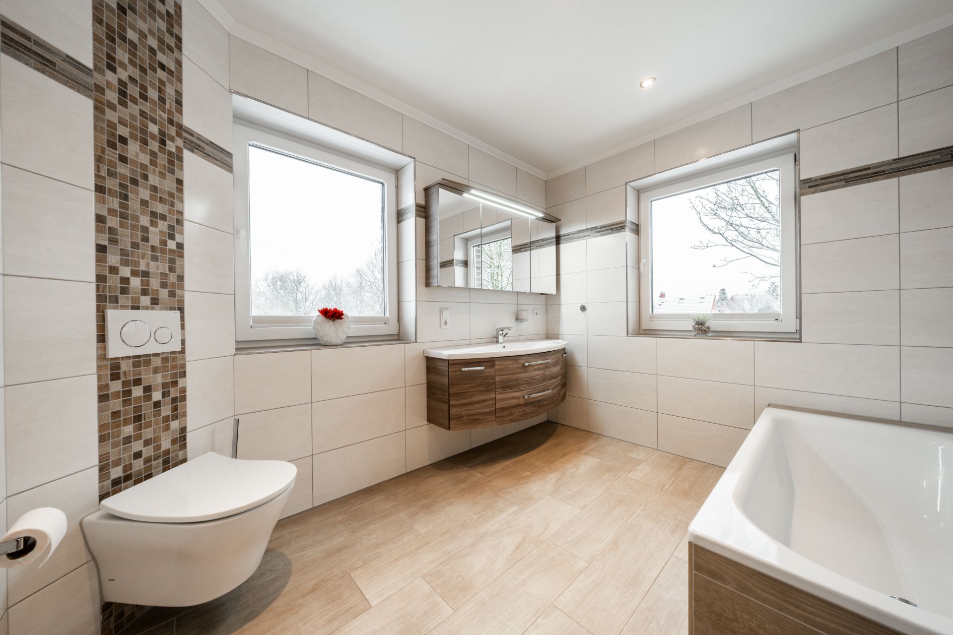 Modernes Badezimmer mit zwei Fenstern, Hänge-WC, Waschbecken, Spiegel und Badewanne.