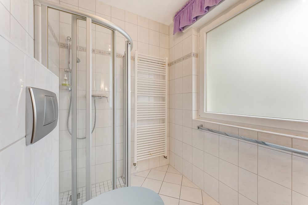Helles Bad mit Dusche, Handtuchheizkörper und großem Fenster mit Milchglas.