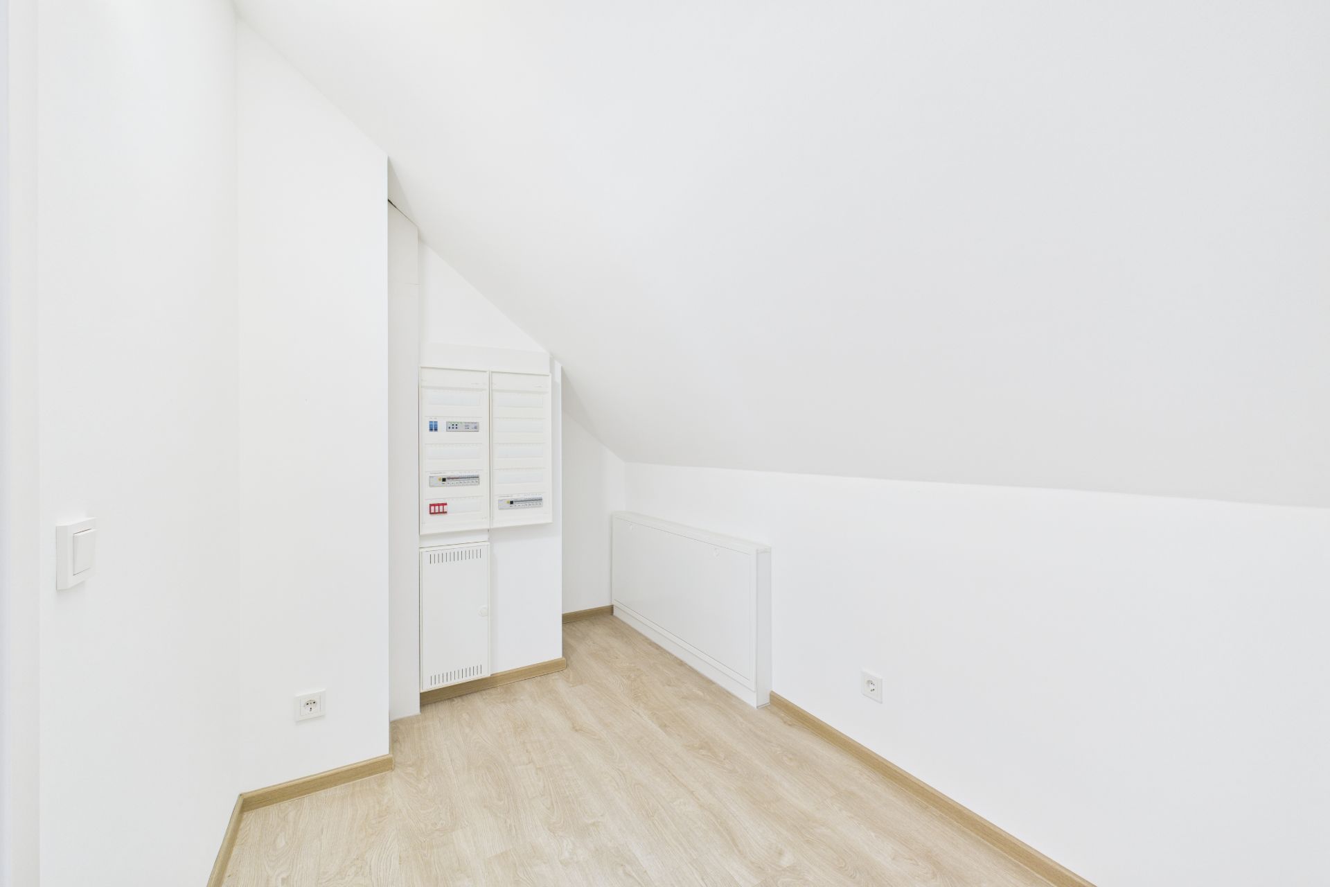Heller Raum mit schräger Decke, weißem Wandschrank und hellem Holzboden.