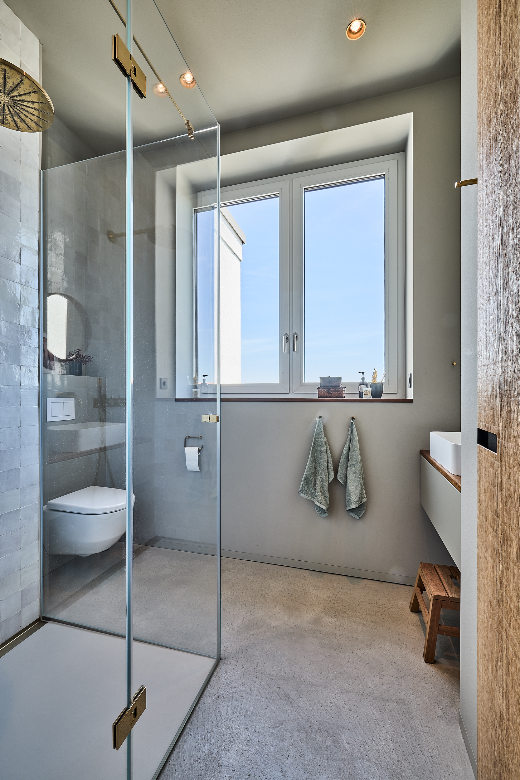 Modernes Badezimmer mit Glasdusche, Toilette, Waschbecken und großem Fenster.