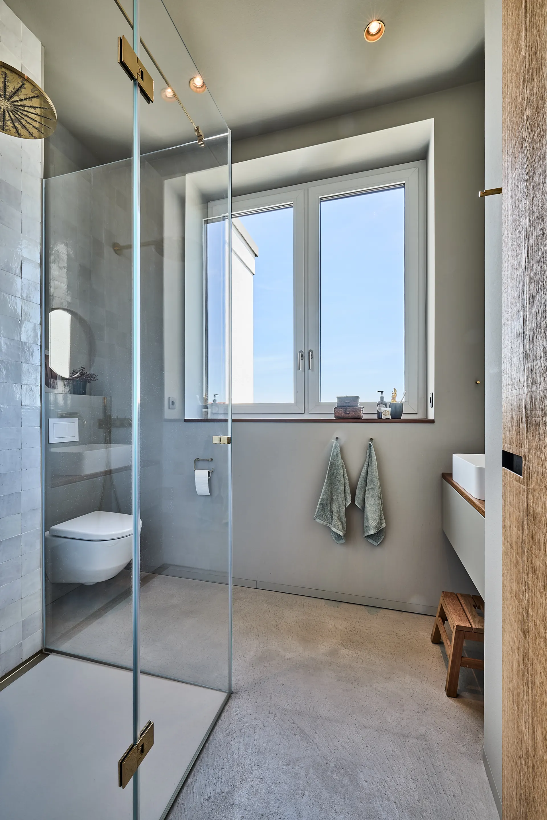 Modernes Badezimmer mit Glasdusche, Toilette, Waschbecken und großem Fenster.