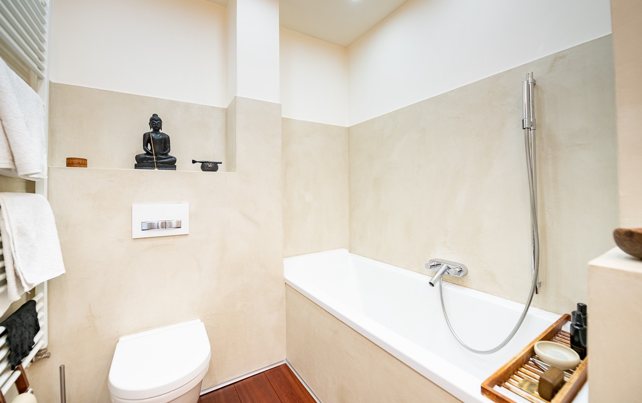 Modernes Badezimmer mit Badewanne, WC und Handtüchern, dekoriert mit Buddha-Figur.