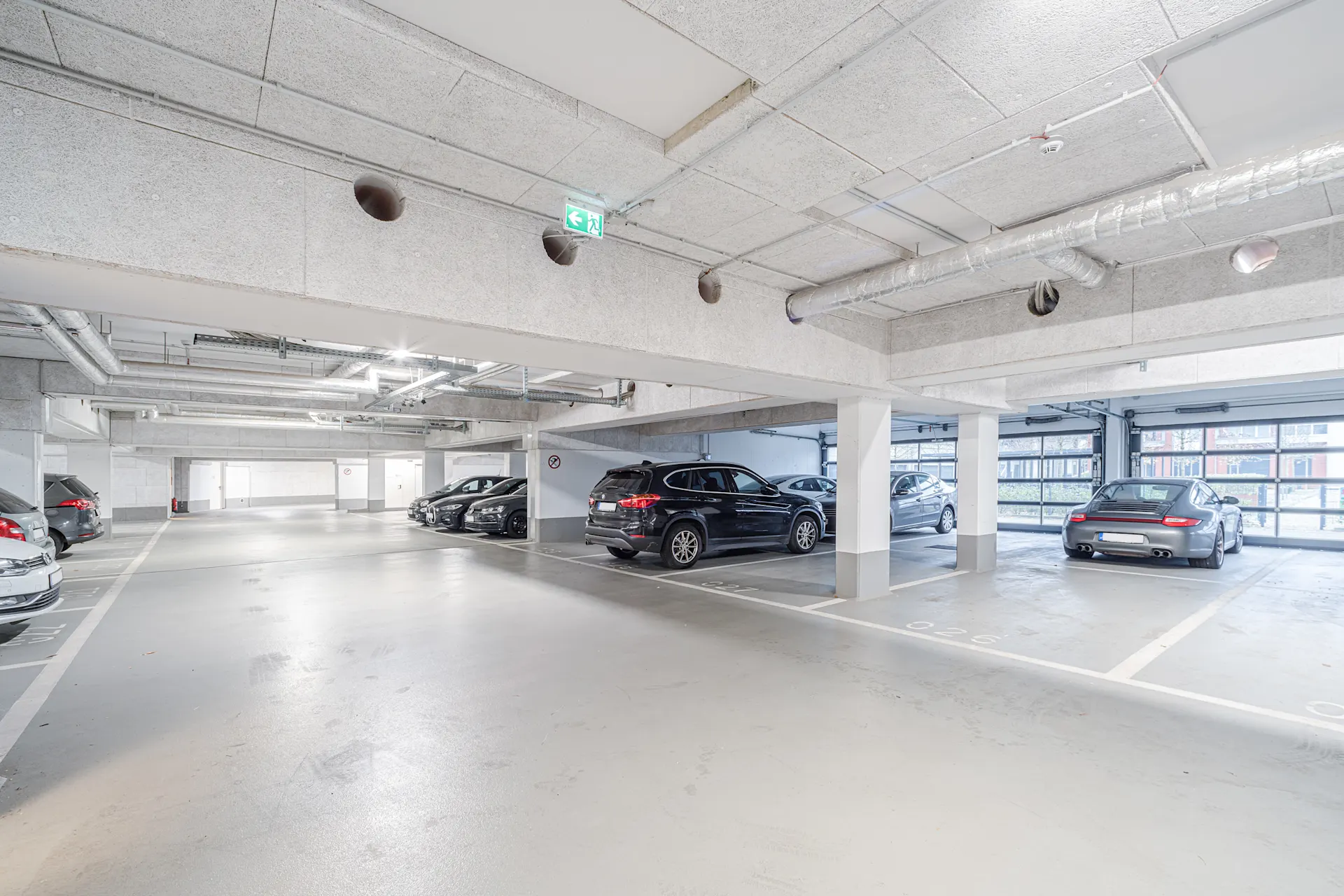 Helle Tiefgarage mit geparkten Autos und sichtbaren Parkplätzen.