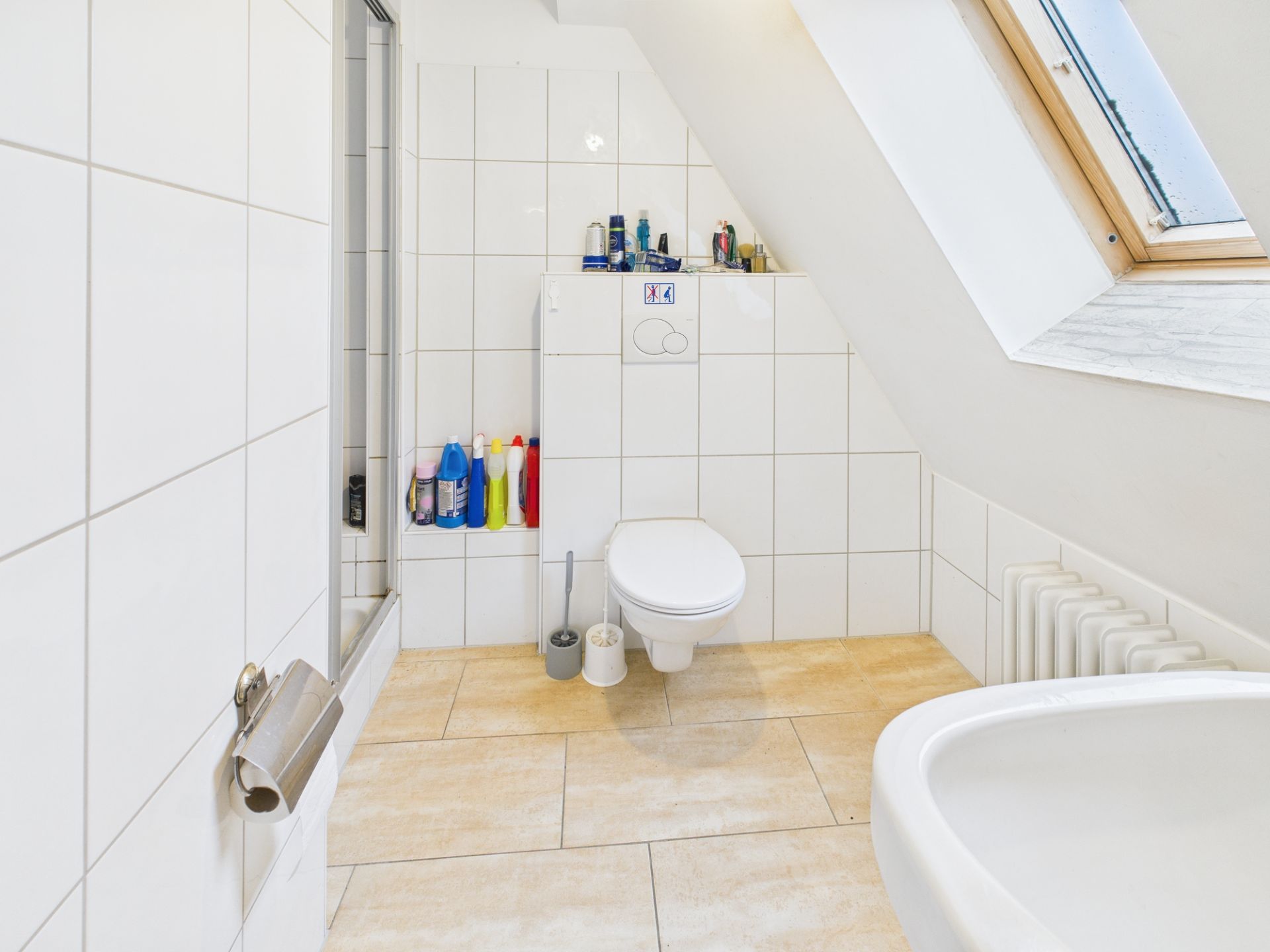 Modernes Badezimmer mit WC, Waschbecken, Fliesen, Putzmitteln und Dachfenster.