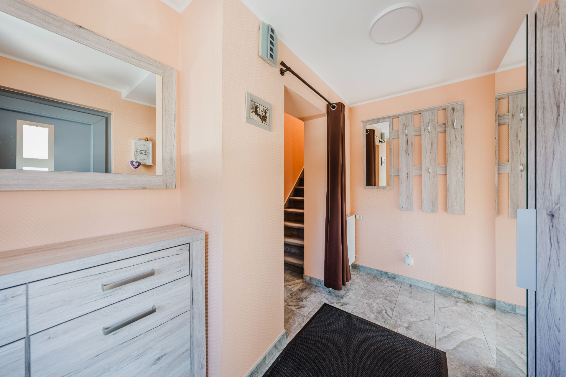 Heller Flur mit Spiegel, Garderobe, Kommode und Blick auf eine Treppe.