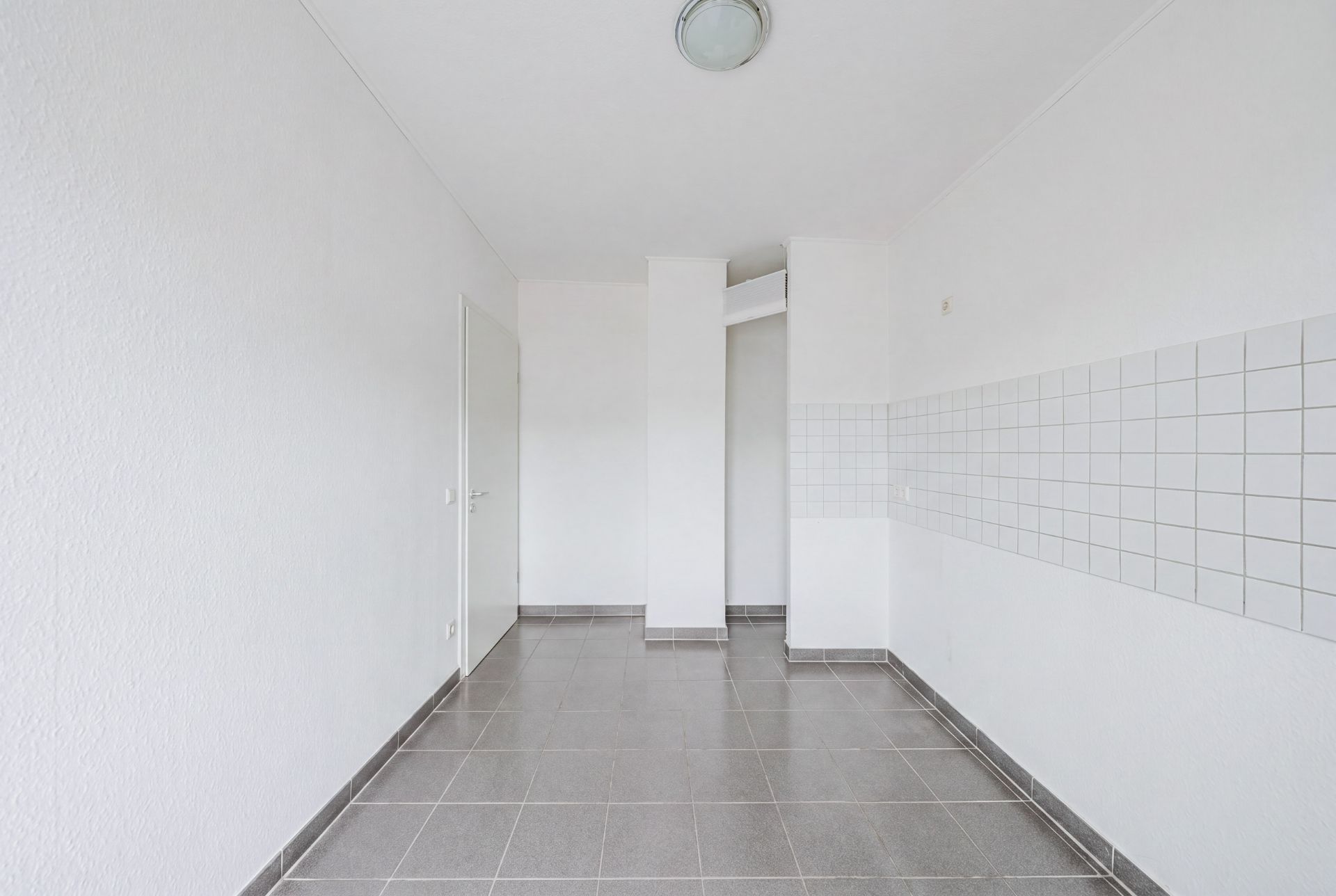 Leerer, weißer Raum mit grauen Fliesen und Fliesenspiegel an der Wand.