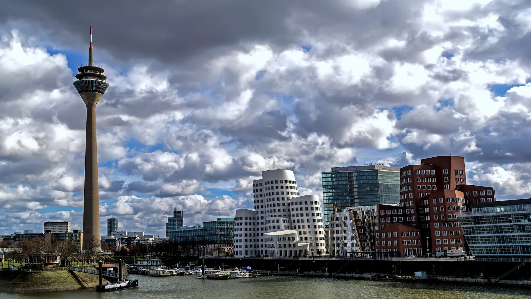 Stadtsilhouette mit modernem Fernsehturm und ungewöhnlich geformten Gebäuden am Wasser.